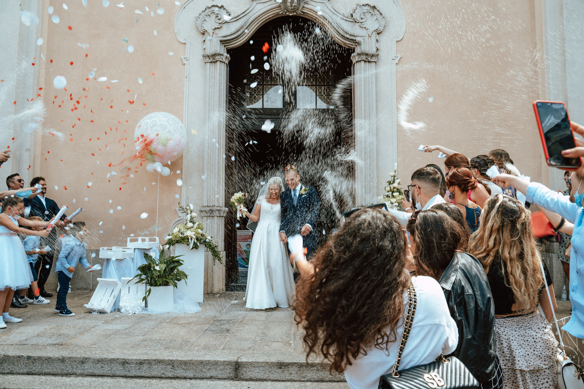 Lancio di riso e petali sugli sposi all'uscita della chiesa tra gli invitati, matrimonio reportage